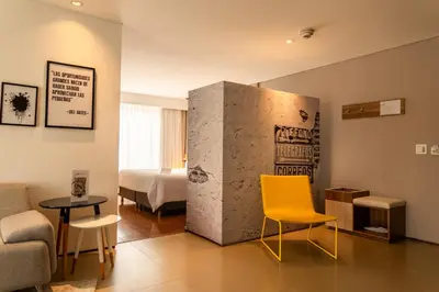 a living room with a yellow chair and a room with a bed at Quo Quality Hotel in Manizales