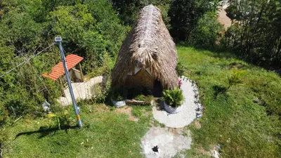 a small house with a straw roof on a field at Cabaña Glamping vista verde Cocorna in Cocorná
