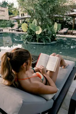 a girl in a bikini reading a book next to a swimming pool at La Gracia Hotel & Spa in San Jerónimo