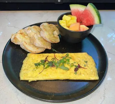 a black plate with an omelet and a bowl of fruit at Hotel Living 35 Suites Piso 8 Vip in Medellín