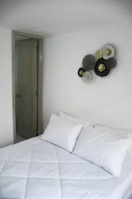 a white bed with white pillows and a clock on the wall at Divino Apartamento Moderno con la Mejor Ubicación in Manizales