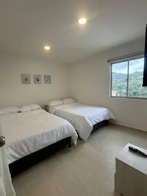 two beds in a white room with a window at Apartamento acogedor cerca al Cable in Manizales