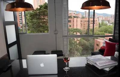 a glass of wine and a laptop on a table with a window at EXCLUSIVO APARTAMENTO para disfrutar Medellin in Medellín