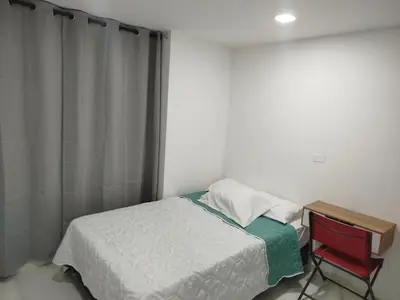 a small bedroom with a bed and a red chair at Apartamento en Belén in Medellín