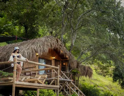 a woman sitting on a porch of a thatch hut at Glamping Caribe con bar y bañera privada in Sopetran