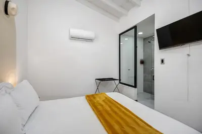 a white bedroom with a large bed and a television at MAKONDO - Large Jacuzzi and AC on Main Provenza St in Medellín
