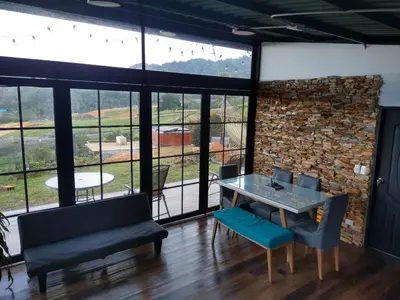 a dining room with a table and chairs and large windows at Chalet las palmas Poblado in Medellín