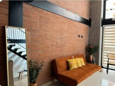 a brown couch with two yellow pillows on a brick wall at Hermoso Loft in Medellín