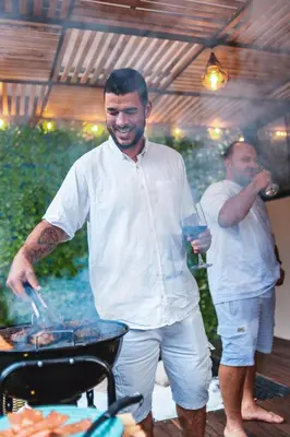 a man cooking food on a grill with a glass of wine at Cabaña Montecielo San Rafael in San Rafael