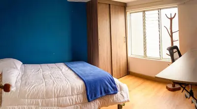 a bedroom with a bed with a blue wall and a window at Corazón Verde in Itagüí