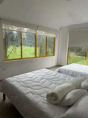 a white bedroom with two beds and a window at Alojamiento con vista al río y paisajes hermosos in Manizales