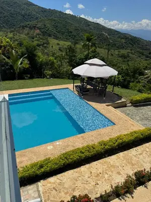 a blue swimming pool with an umbrella and a table at Paraíso in San Jerónimo