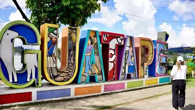 a woman walking past a display of the word art at Las Casas de Tomate in Guatapé
