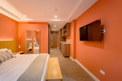 a bedroom with an orange wall with a bed and a flat screen tv at El Tesoro Escape Modern & Cozy Room 303 in Medellín