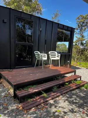 a black tiny house with two chairs and a wooden deck at Tiny House Minimalista en la Naturaleza cerca a El Retiro y La Ceja in El Retiro