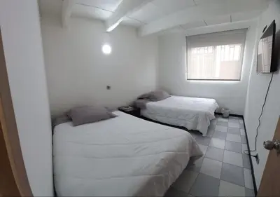 two beds in a white room with a window at Hospedaje Gladys in Manizales