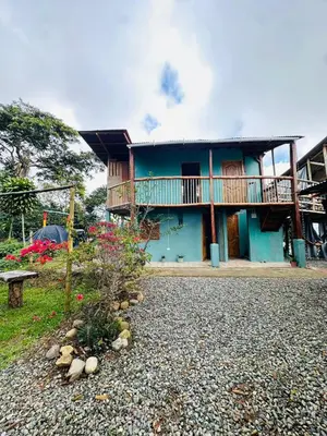 a blue house with a balcony and a gravel yard at Titiribi-Antioquia- Cabaña el sol in Titiribí