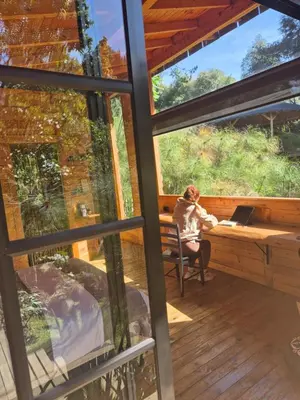 a woman sitting at a desk in a house with a window at Cabaña Silencio in Guarne