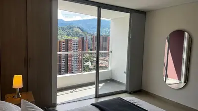 a bedroom with a large window with a mountain view at Apartasuite Sabaneta Vista a la ciudad parking in Sabaneta