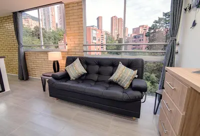 a black couch in a living room with a large window at Staynova loft acogedor en El Poblado, Medellín in Medellín