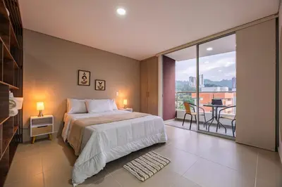 a bedroom with a bed and a balcony with a table at Apartasuite Sabaneta City view parking in Sabaneta
