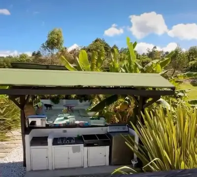 a barbecue grill with a green roof in a garden at Cabaña Blanca Cielo Abierto in Guarne