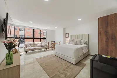 a white bedroom with a bed and a living room at 41 Experience Laureles in style and comfort in Medellín