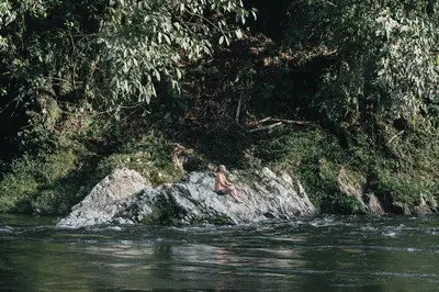 a man is sitting on a rock in the water at Casa blanca, Refugio Natural Jacaranda in Cocorná