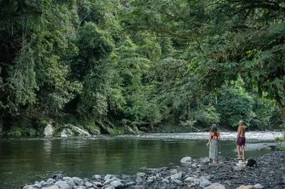 two people standing on rocks near a river at Casa blanca, Refugio Natural Jacaranda in Cocorná