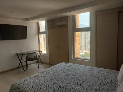 a bedroom with a bed and a table and two windows at Laureles Deluxe Apartment in the Medellin sky in Medellín