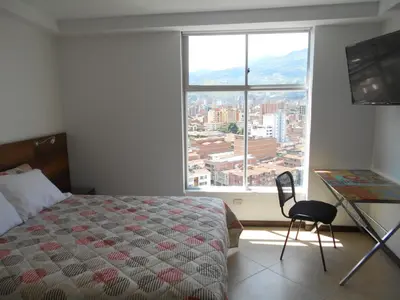a bedroom with a bed and a desk and a large window at Laureles penthouse, jacuzzi-rooftop fun in the sun in Medellín