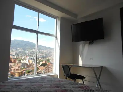 a bedroom with a bed and a desk and a large window at Laureles penthouse, jacuzzi-rooftop fun in the sun in Medellín