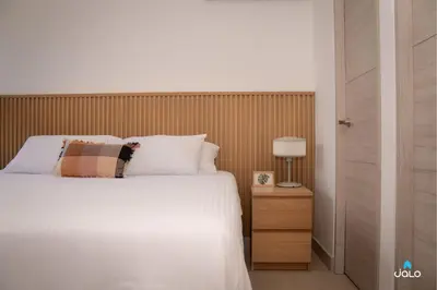 a bedroom with a white bed and a wooden headboard at Grand By Jalo in Medellín