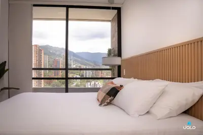 a bedroom with a white bed with a large window at Grand By Jalo in Medellín
