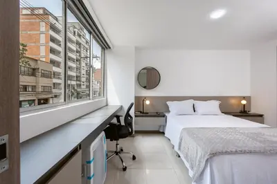 a bedroom with a bed and a desk and a window at Mirador Verde by MOME in Medellín