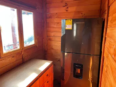 a refrigerator in a wooden cabin with two windows at Cabaña Selvática y Manantiales, San Miguel Guarne in Guarne