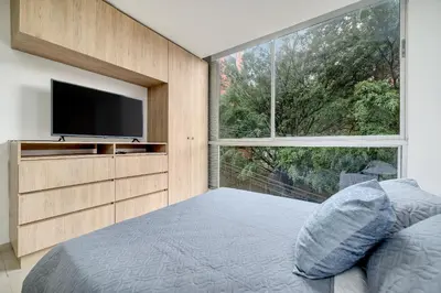 a bedroom with a large window and a television at Apartamentos Oslo Tesoro by HOUSY in Medellín