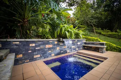 a pool in a garden with a stone wall and a fountain at Hermosa Casa y Cabañas en Barbosa, Antioquia in Barbosa