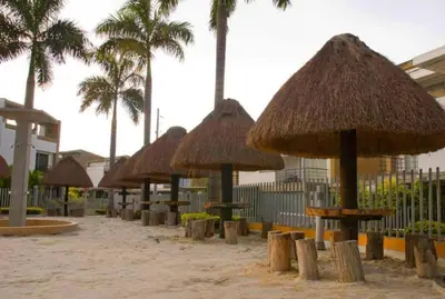 a row of straw umbrellas on a beach with palm trees at Cabaña ciudadela premium San Jerónimo in San Jerónimo