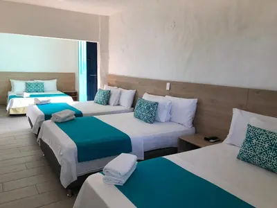 a hotel room with three beds with blue and white pillows at Hotel Aldea Plaza in Doradal