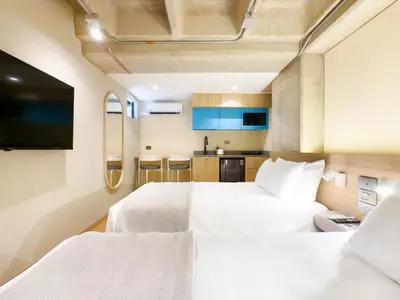 a bedroom with two white beds and a kitchen at Hotel Once22 in Sabaneta