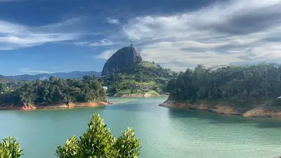 a mountain sitting on top of a river with trees at Balcones Guatape Apartment in Guatapé