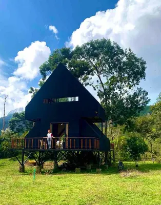 a man standing on the porch of a black house at Cabaña del rio, San Luis, Antioquia in San Luis