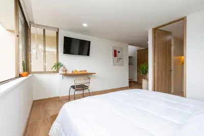 a bedroom with a large white bed and a chair at Laureles Apt-Big Windows-Smart lock- AC in Medellín
