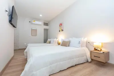 a white bedroom with two beds and a television at Spacious Apt -Laureles -AC -Smart Lock- WiFi in Medellín