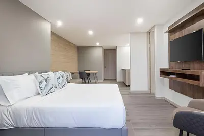 a bedroom with a white bed and a flat screen tv at Class 48 Apt. 2301 - Luces de ciudad/Loft/Balcón priv in Sabaneta