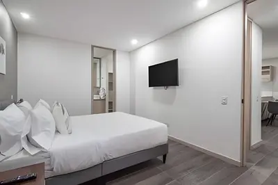 a white bedroom with a bed and a flat screen tv at Class 48 Apt. 2303 - Loft de alta clase -balcón privado in Sabaneta