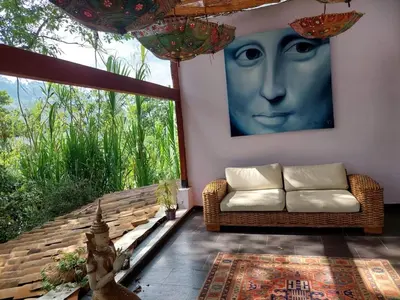 a living room with a couch and a large window at Artsy lush villa with jungle garden in the city in La Estrella