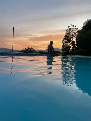 a man sitting next to a swimming pool at sunset at Finca, piscina y sin limite de sonido en Sopetran in Sopetran
