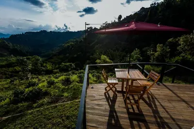 a table and chairs on a deck with an umbrella at Moonshine - Sereno Glamping in Manizales